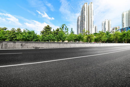 Freshly paved asphalt road with white lane markings and city buildings.