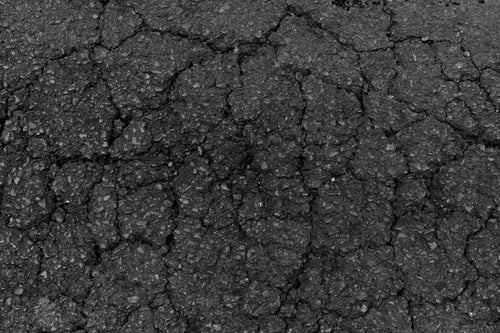 Close-up of hairline cracks spreading across asphalt pavement.